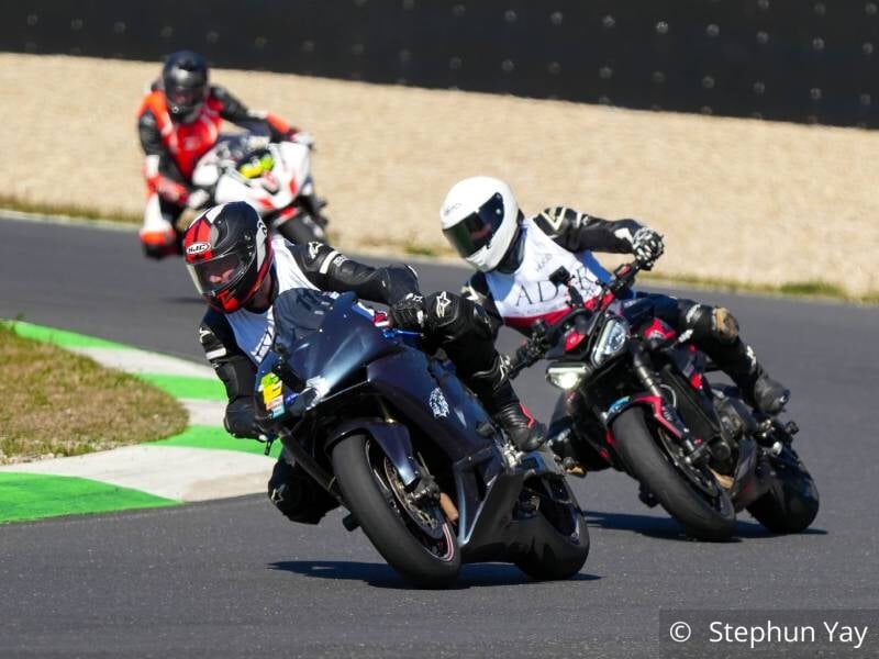 Trois pilotes de moto sur un circuit, dans un virage, deux au premier plan et un au second